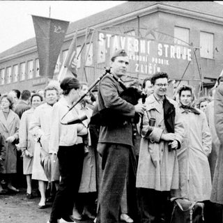 People gather in front of a building with Soviet symbols, likely during Cold War era.
