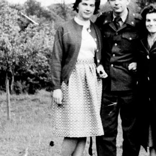 Three individuals in mid-20th-century attire posing outdoors.