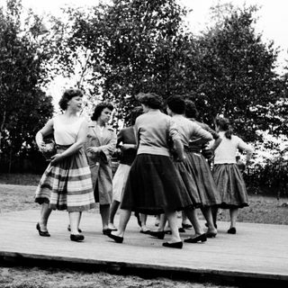 Group of women dancing in 1950s-style skirts outdoors.