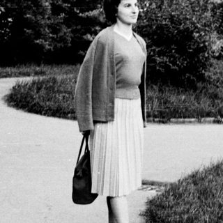 Woman walking alone in park on paved path.