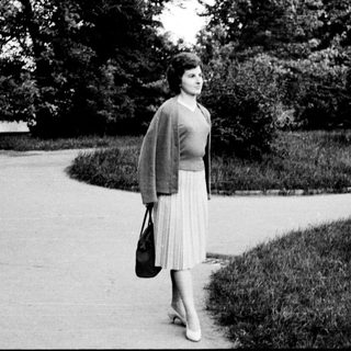 Woman walking alone in park on paved path.