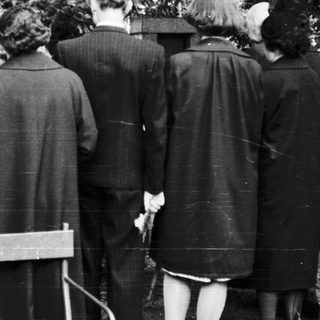 Group of people standing at gravesite in cemetery.