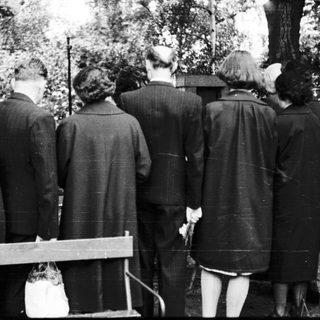 Group of people standing at gravesite in cemetery.