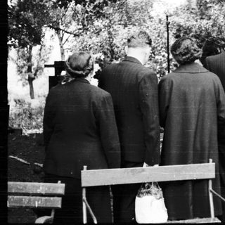 Group of people standing at gravesite in cemetery.