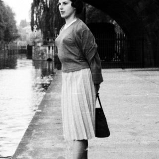 Woman standing under bridge by canal.