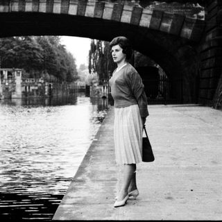 Woman standing under bridge by canal.