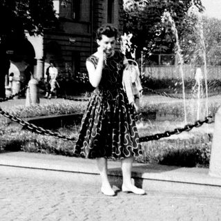Vintage park scene with woman in 1950s dress near fountain.