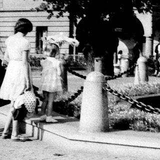 Vintage park scene with woman in 1950s dress near fountain.