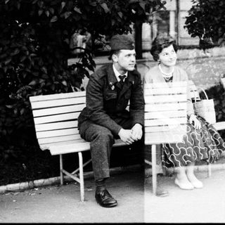 Two people sitting on park benches, likely mid-20th century.