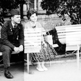 Two people sitting on park benches, likely mid-20th century.