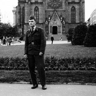 Man in military uniform standing outdoors near cathedral.
