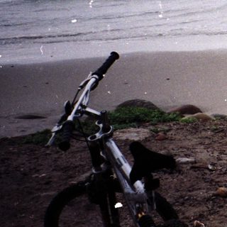 Man standing on beach near ocean with bicycle.