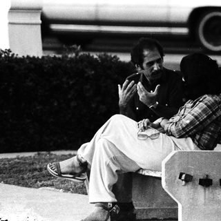 Two men sitting on a bench outdoors.