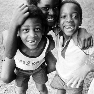 Three smiling children posing outdoors together.