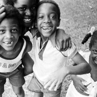 Three smiling children posing outdoors together.