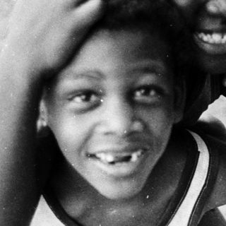 Three smiling children posing outdoors together.