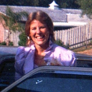 Woman smiling from car roof, suburban driveway.