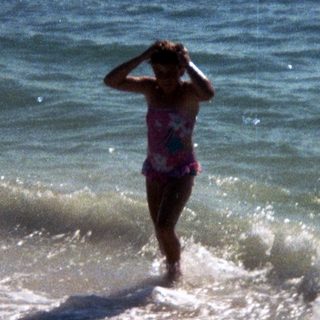 Woman in bikini standing in shallow ocean waves.
