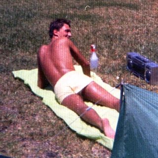 Shirtless man relaxing on towel outdoors.