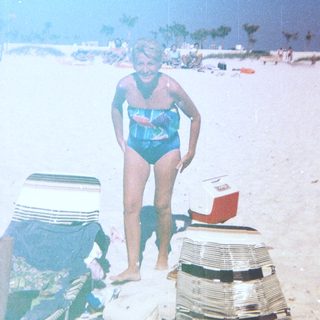 Person in blue swimsuit at beach with cooler.