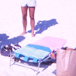 Beach scene with man holding camera, woman standing nearby.