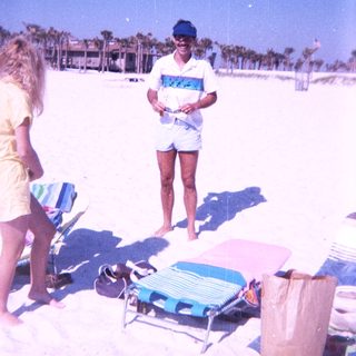 Beach scene with man holding camera, woman standing nearby.