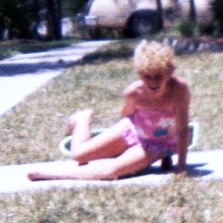 Child sitting on dry grass near sidewalk.