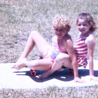 Two young girls sitting on sidewalk in backyard.