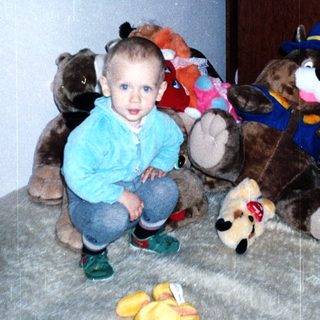 Here's a brief summary of the image: Young boy sits surrounded by several stuffed animals.