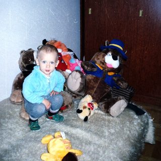 Here's a brief summary of the image: Young boy sits surrounded by several stuffed animals.