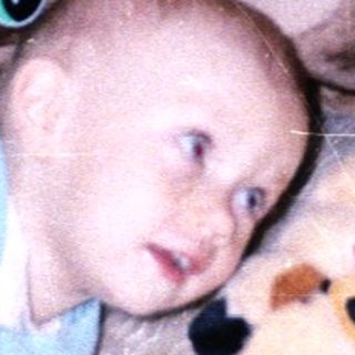 Baby lies on a rug surrounded by stuffed animals.