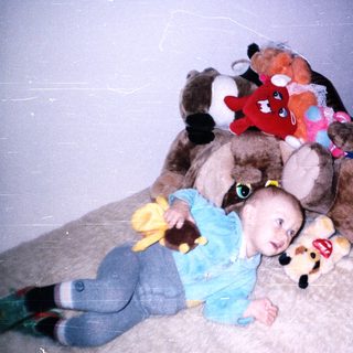 Baby lies on a rug surrounded by stuffed animals.