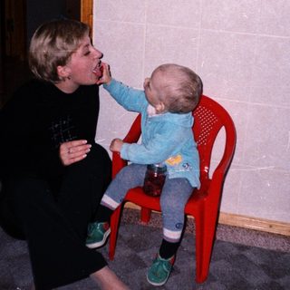 A person feeds a baby sitting on a chair.
