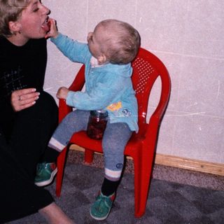 A person feeds a baby sitting on a chair.