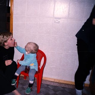 A person feeds a baby sitting on a chair.