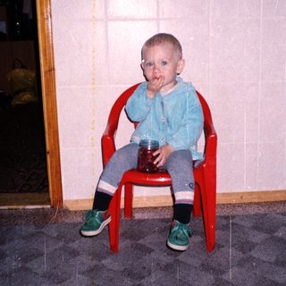 Baby sitting in a chair, covered in red substance.