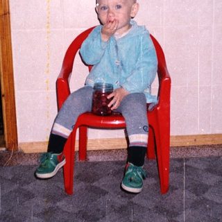 Baby sitting in a chair, covered in red substance.