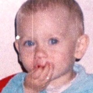 Baby sitting in a chair, covered in red substance.