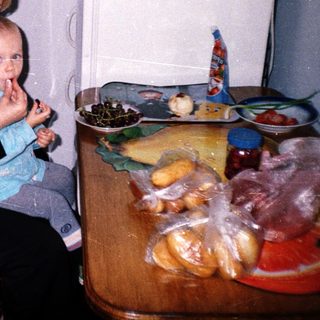Woman sits holding a baby near a food-filled table.
