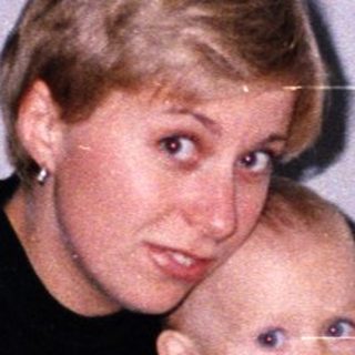 Woman sits holding a baby near a food-filled table.