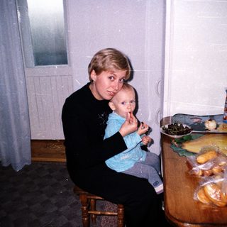 Woman sits holding a baby near a food-filled table.
