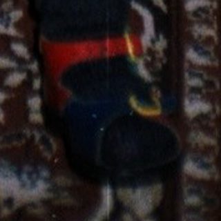 Baby in patterned clothing stands, with adults nearby.