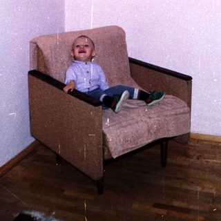 A young child sits in a chair indoors.