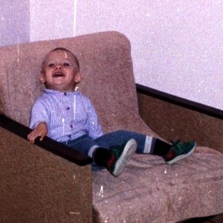 A young child sits in a chair indoors.