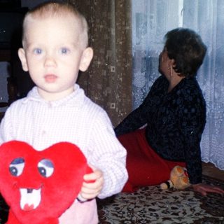 Toddler holds a heart-shaped toy, with adults in background.