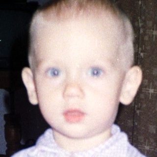 Toddler holds a heart-shaped toy, with adults in background.