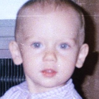 Baby holding toy, standing near a woman and curtains.