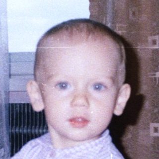 Baby holding toy, standing near a woman and curtains.