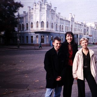 Three people stand in front of a large building.