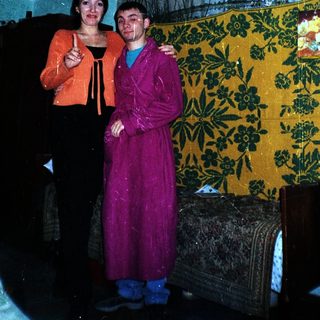Two people standing together in a room with a tapestry.